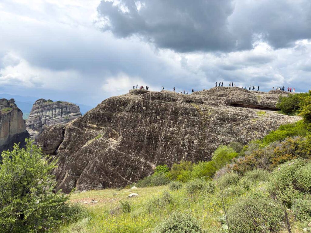 a large crowd of tourists on the Kalabaka Valley Viewpoint in Meteora, Greece.