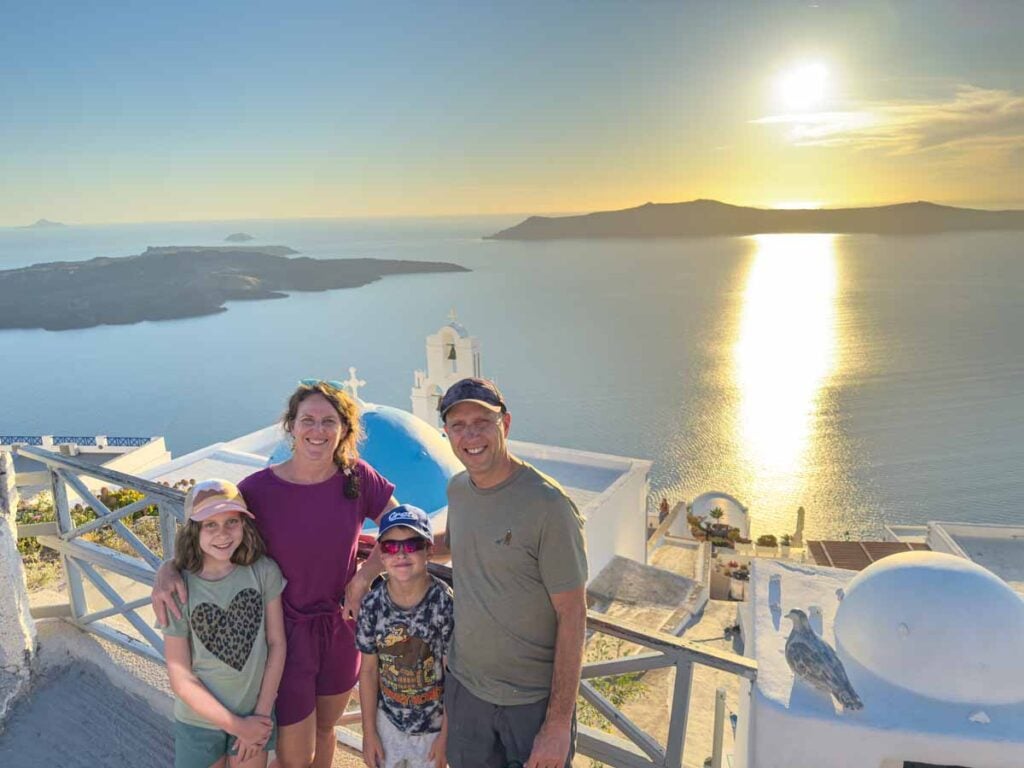 Dan and Celine Brewer, owners of Family Can Travel, watch the sunset while visiting Santorini with kids.