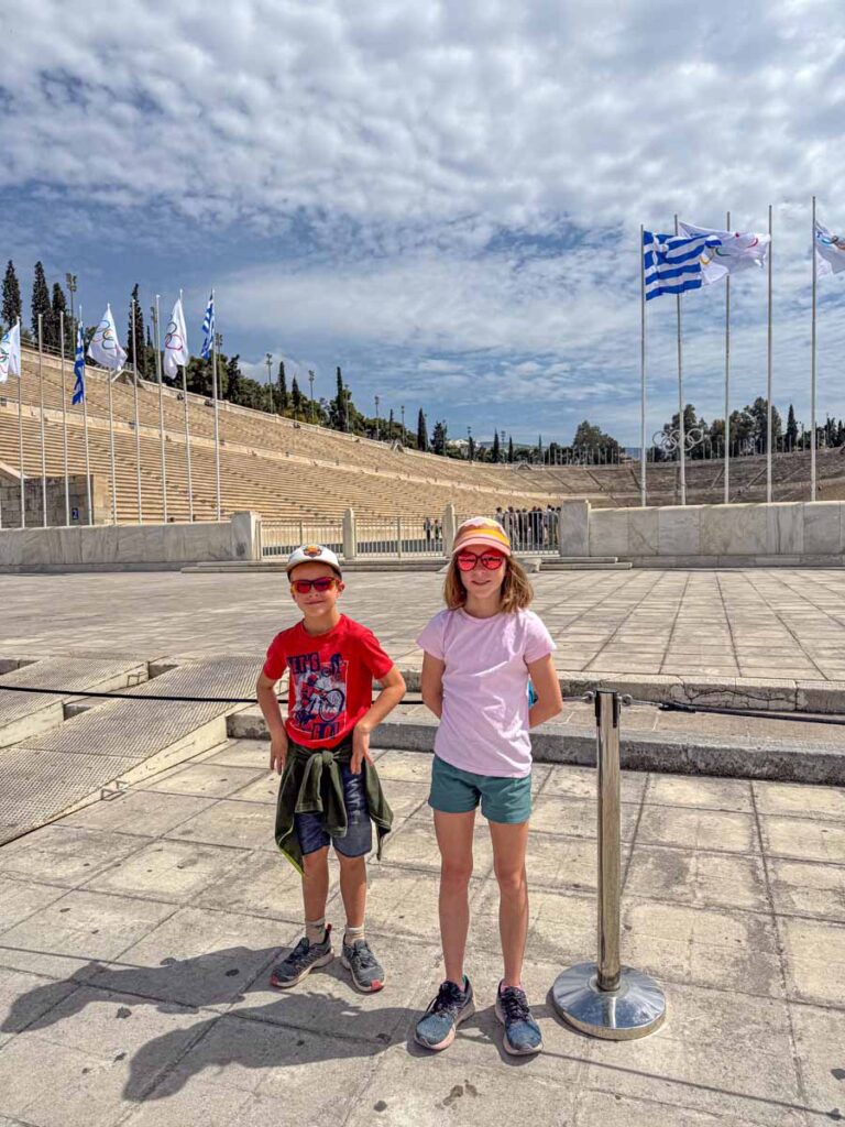 The Brewer kids, from the FamilyCanTravel.com blog, stand outside the Panathenaic Stadium while on a family vacation to Greece.