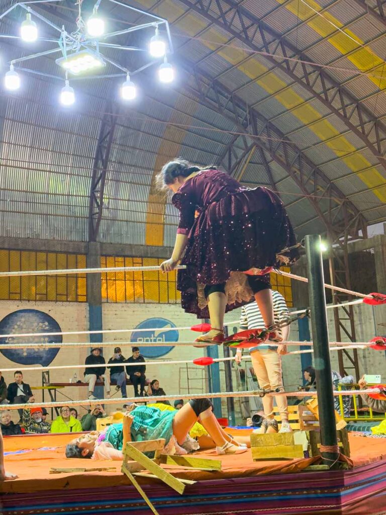 a female Cholitas Wrestler climbs the top rope during a match in El Alto, Bolivia (near La Paz).
