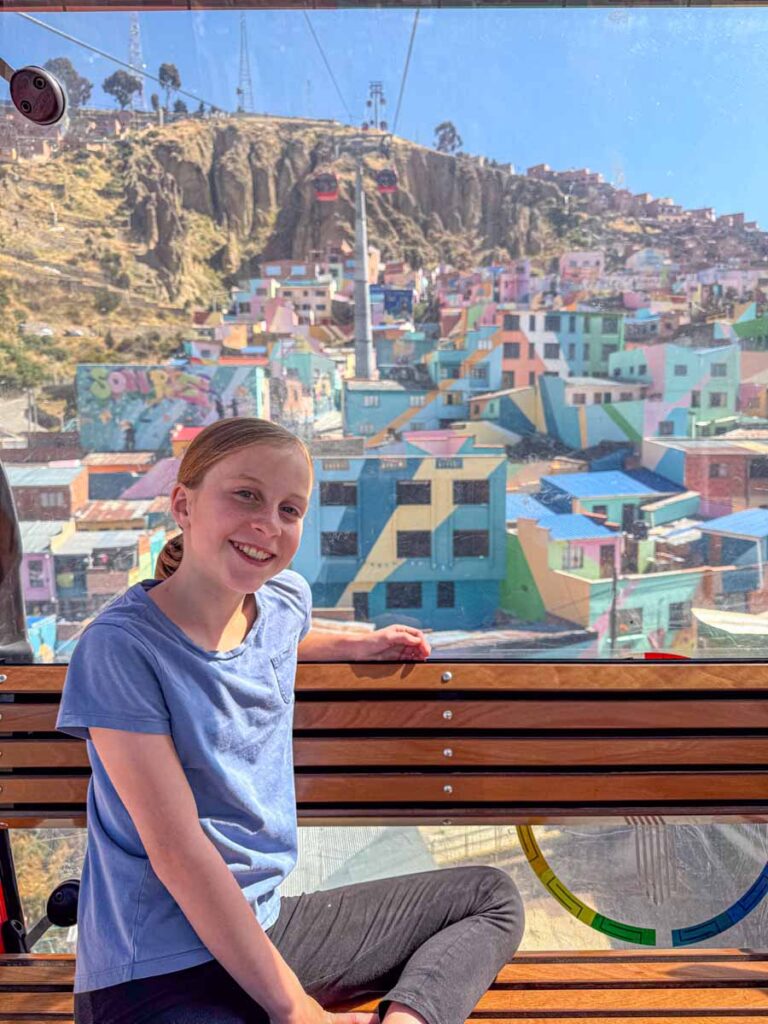 an 11-year old girl enjoys views of the colorful Chualluma neighborhood while riding a red cable car on a family trip to La Paz, Bolivia.