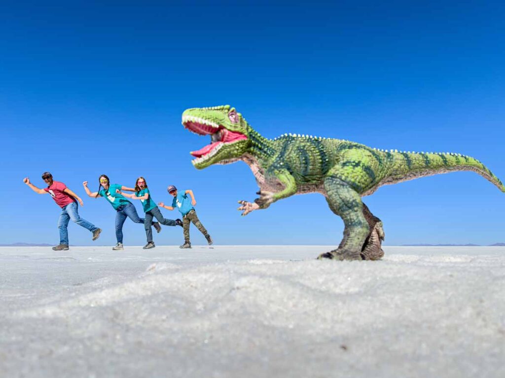 Dan and Celine Brewer, owners of FamilyCanTravel.com, pose for a fun forced perspective photo with their kids and a giant T-Rex in the Uyuni Salt Flats, Bolivia.