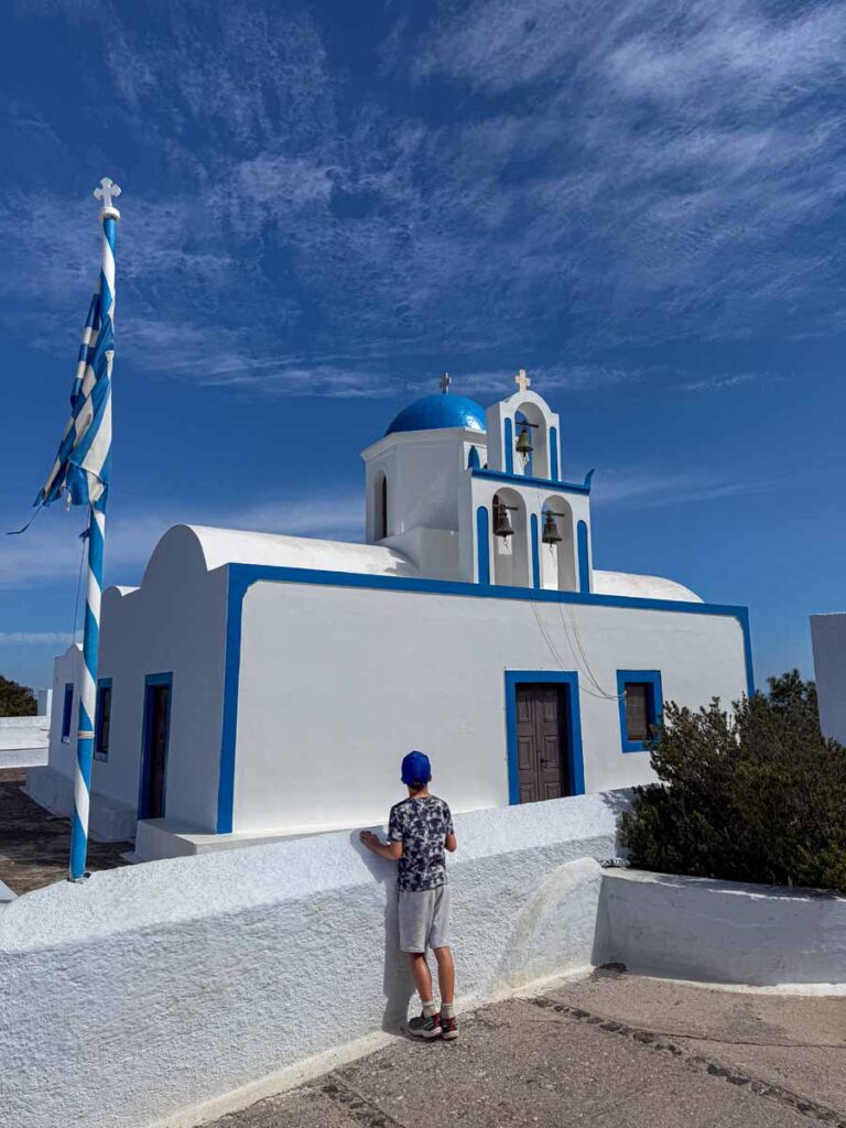 A 9-year old boy stops to admire a whitewashed church with classic Greek blue trim while on a family trip to Santorini, Greece.
