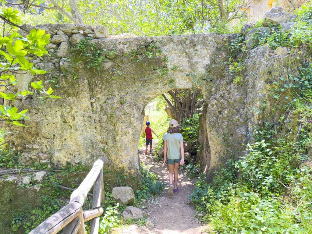 two kids hike under an archway on the Mili Gorge hike in Crete, Greece.