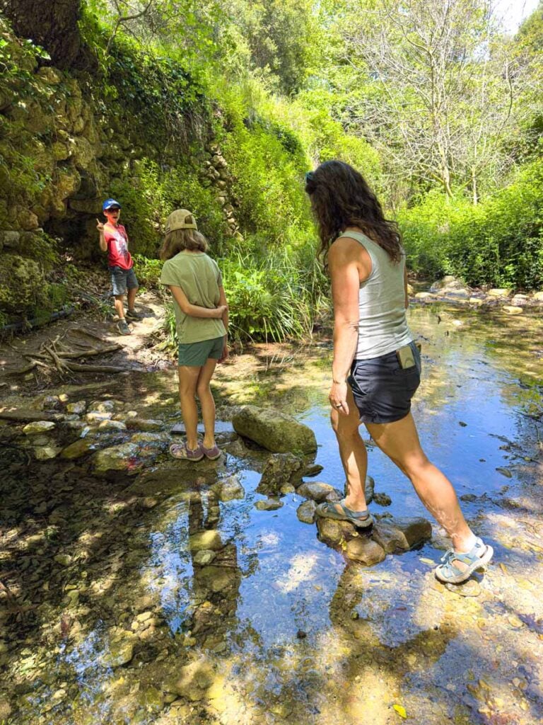 Celine Brewer and her kids cross a stream on some rocks while hiking the Mili Gorge trail on a family vacation to Crete, Greece.