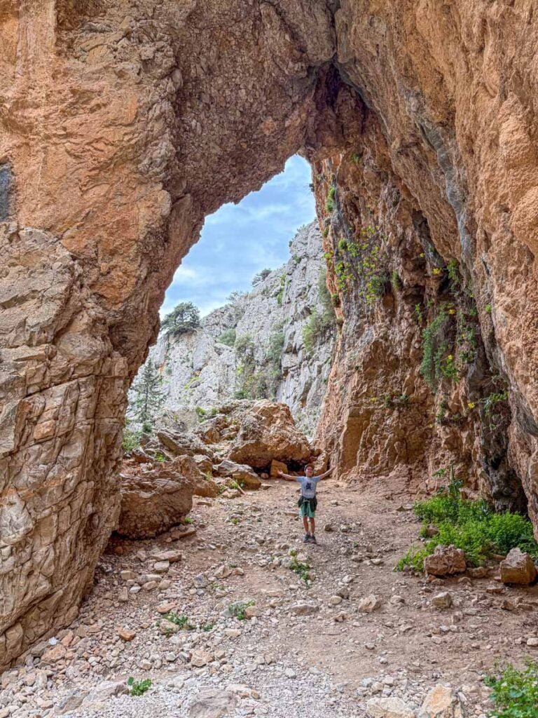 a 9-year old boy stands under a natural archway on the Imbros Gorge Hike in Crete, Greece.