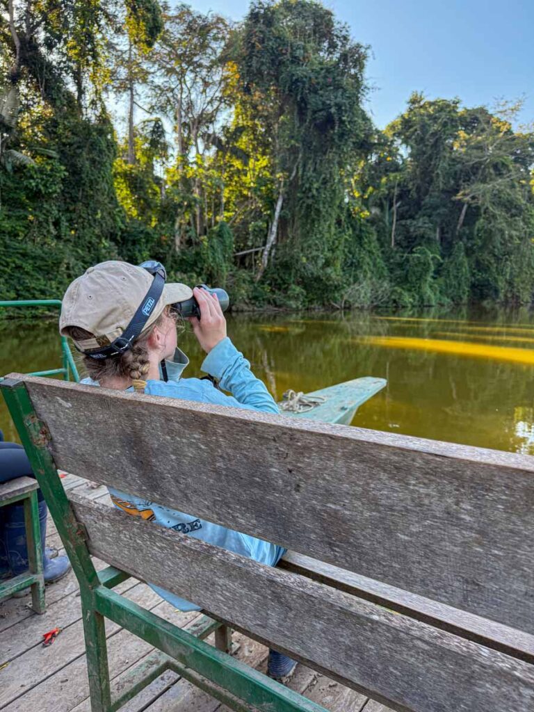 A 12-year old girl looks for birds through binoculars while on a catamaran boat ride on Salvador Lake in Manu National Park, Peru.