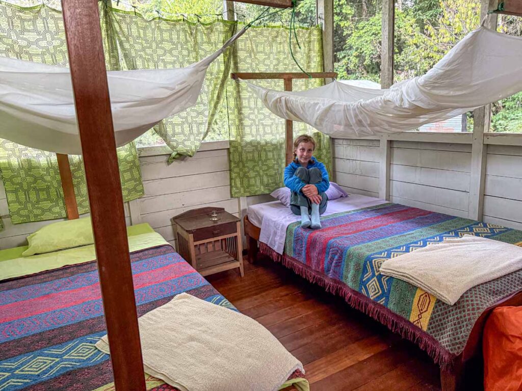 a 12-year old girl sits on her bed at the Hummingbird Lodge while on a family-friendly Manu National Park Tour.