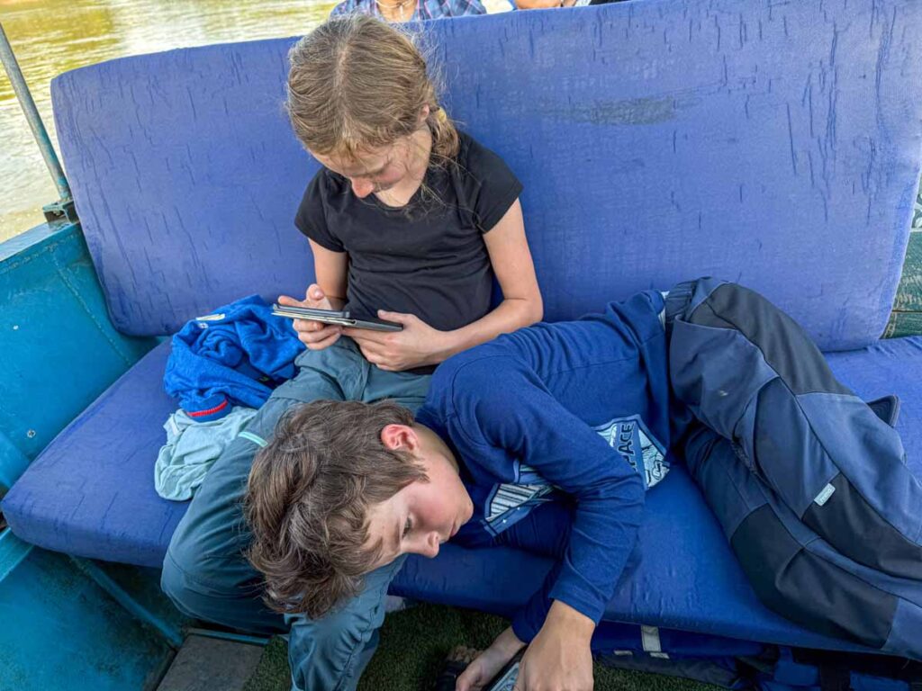 Two kids read on their e-readers during a long boat ride on a family trip to the Amazon jungle in Peru.
