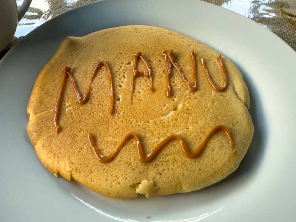 a pancake with the word "Manu" written on it in dulche de leche.