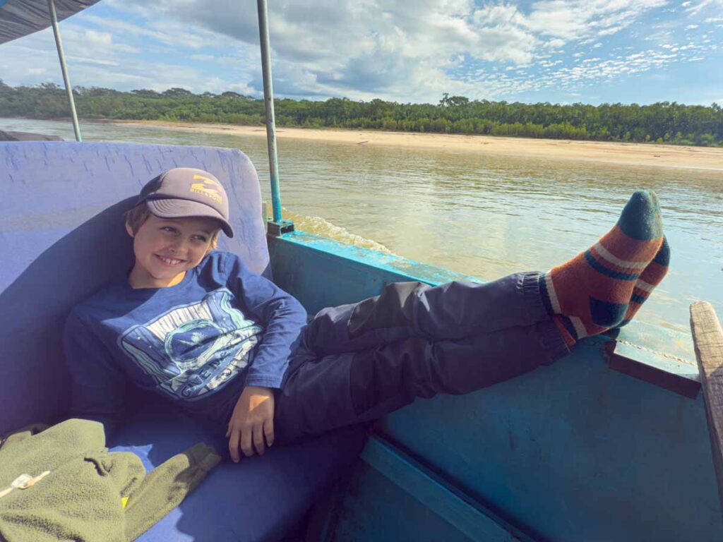 A 9-year old boy kicks back on the boat while spotting wildlife on a Manu National Park tour.