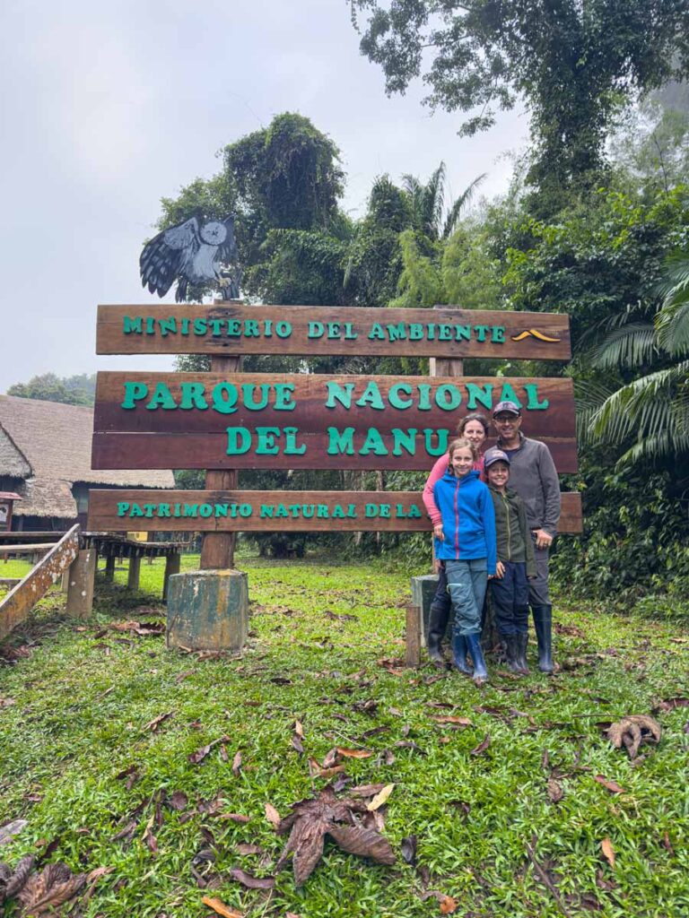 Dan and Celine Brewer, owners of FamilyCanTravel.com, stand with their kids at the entrance sign for Manu National Park at the visitor center.