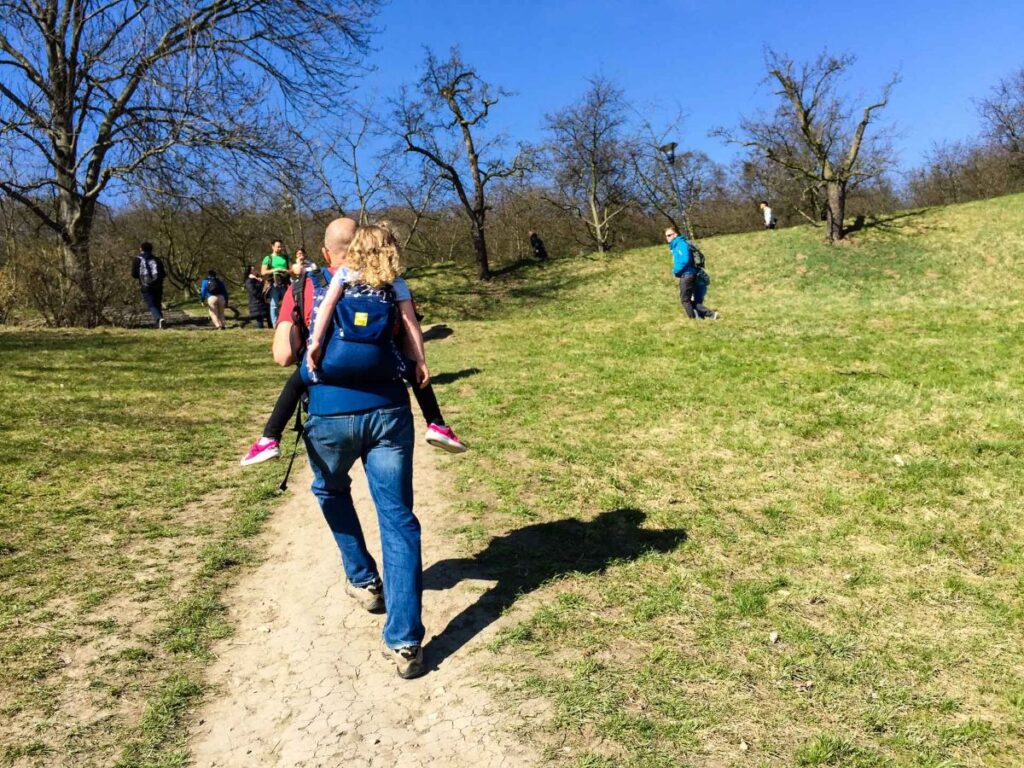 Dan Brewer, owner of FamilyCanTravel.com, carries his young daughter on a family walk in Petrin Park in Prague, Czechia.
