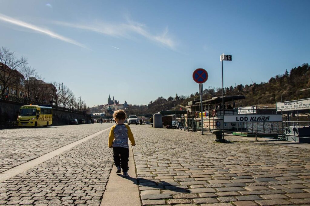 A 2-year old boy walks along the Vltava River on a family trip to Prague.