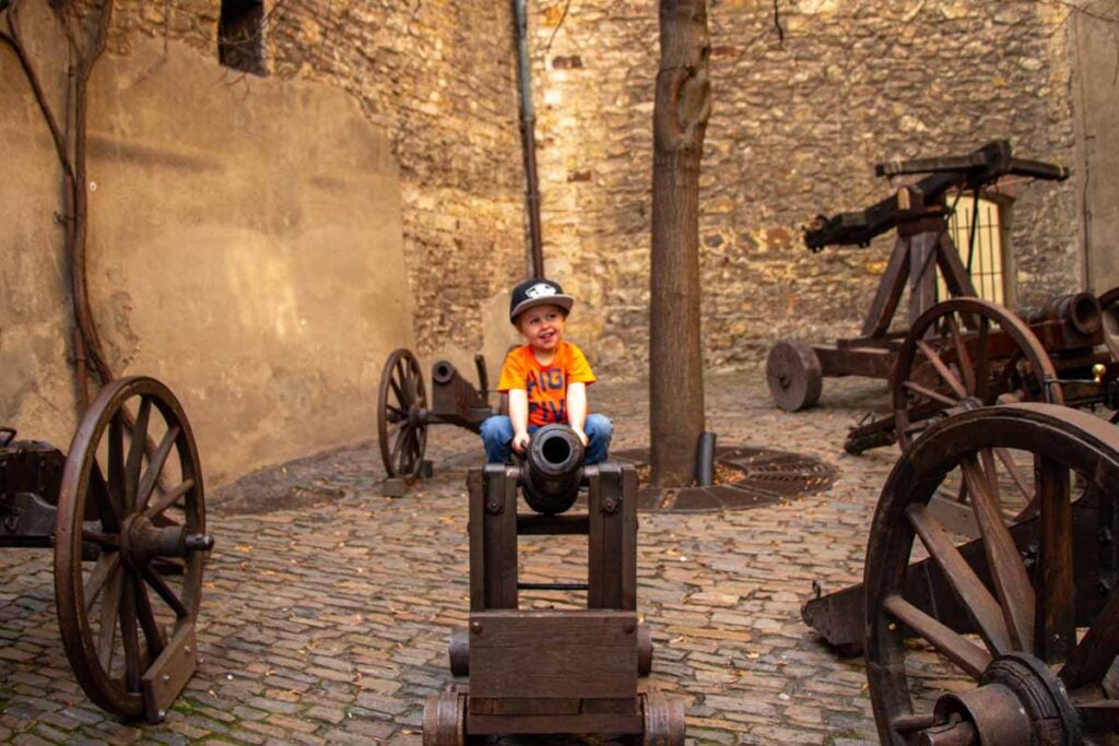 a 2-year old toddler from the Family Can Travel blog, plays on a cannon while visiting Prague Castle with his parents Dan & Celine Brewer.