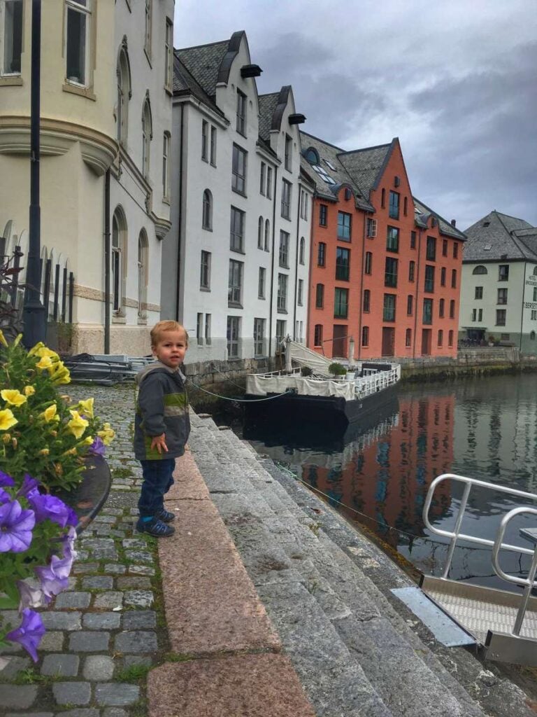 a 2-year old boy stands near some colorful buildings in Alesund's famous Art Nouveau District.