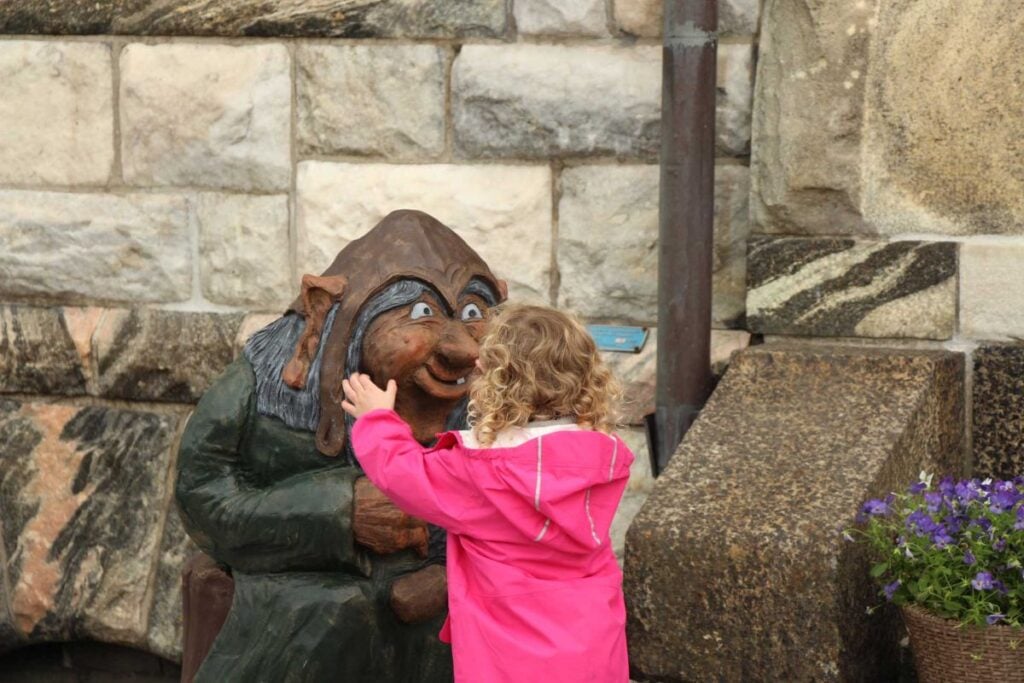 a 4-year old girl on a family trip to Alesund, Norway stops to look at a large wooden troll.