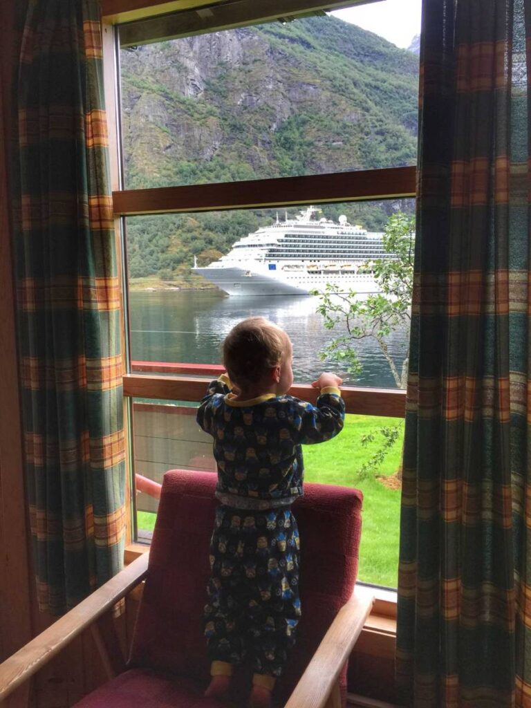 a 2-year old boy watches a cruise ship depart Geiranger from his family-friendly cabin by the water.
