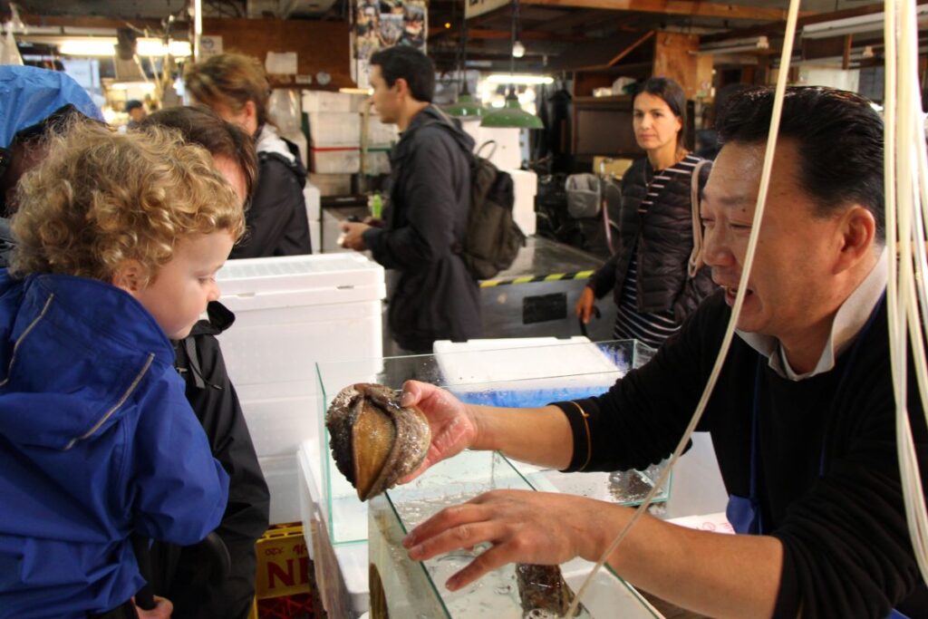 Celine Brewer, owner of FamilyCanTravel.com, holds her daughter to see an interesting shellfish at the Tsukiji Fish Market during a family trip to Tokyo, Japan.