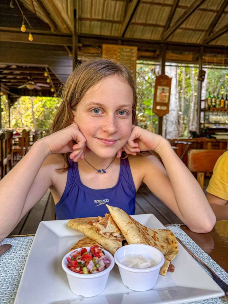 a 12-year old girl on a family trip to the Sweet Songs Lodge, smiles before a meal at the Treehouse Bar.
