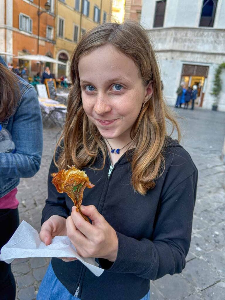 A 12-year old girl tries Carciofi alla Giudia while on a family-friendly food tour of Rome, Italy.