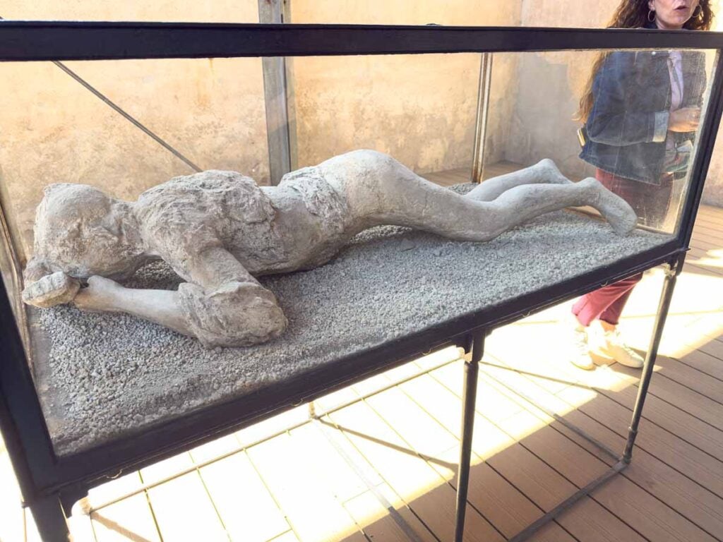a plaster cast body on display near the bathhouse at the Pompeii ruins.