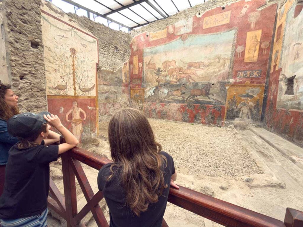 Kids look at the well-preserved artwork in a Pompeii house during a family trip to Italy.
