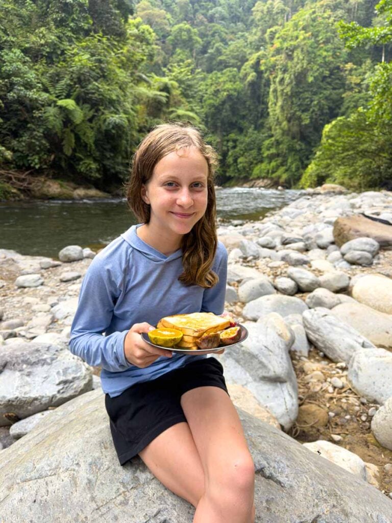 A Brewer child eats breakfast near the river while camping in Gunung Leuser National Park on a family trip to Bukit Lawang.