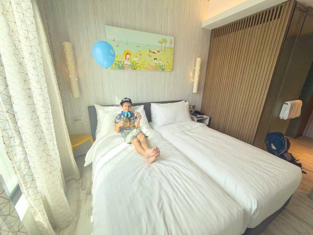 One of the Brewer kids from the Family Can Travel blog, sits on his bed in a Family Room at the Sentosa Singapore Village Hotel.