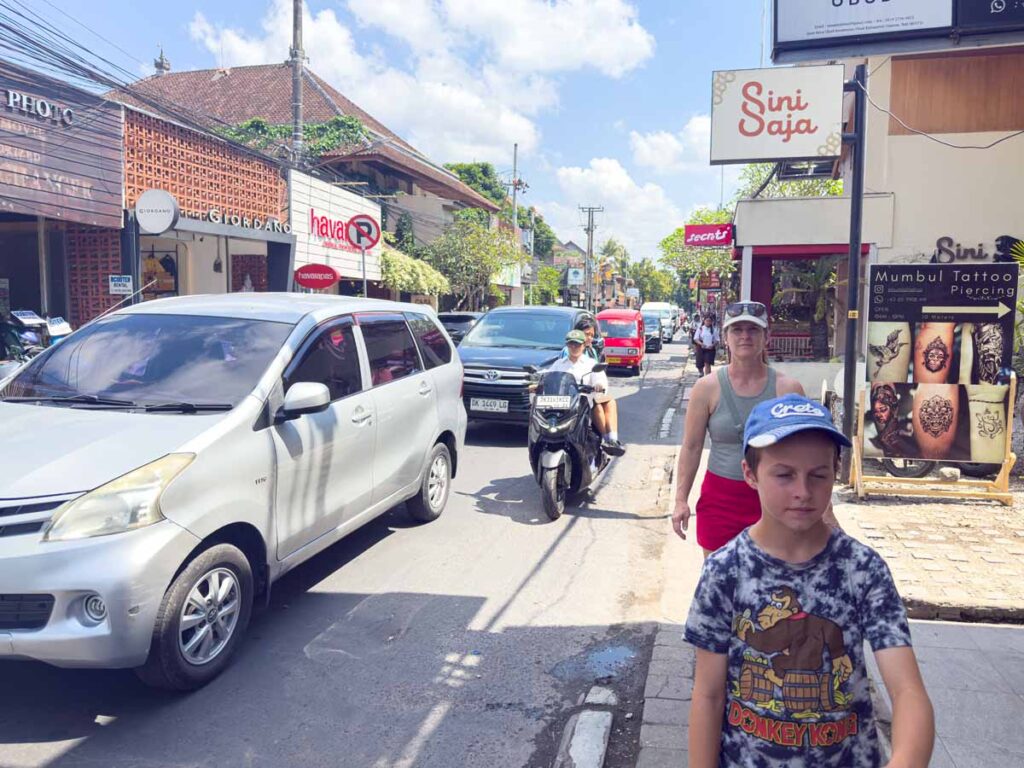 Celine Brewer and her son walk the narrow sidewalks in Ubud, Indonesia with bumper to bumper traffic on the adjacent road.