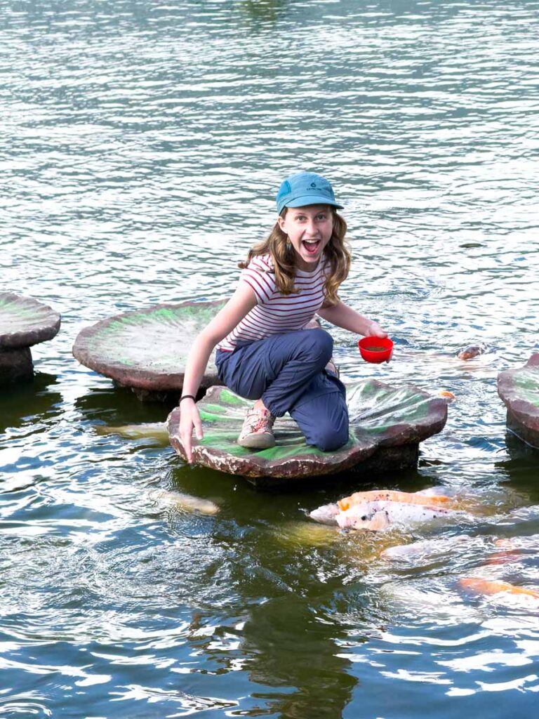 A Brewer child feeds koi fish at the Ulun Danu Beratan temple during a family vacation in Bali, Indonesia.